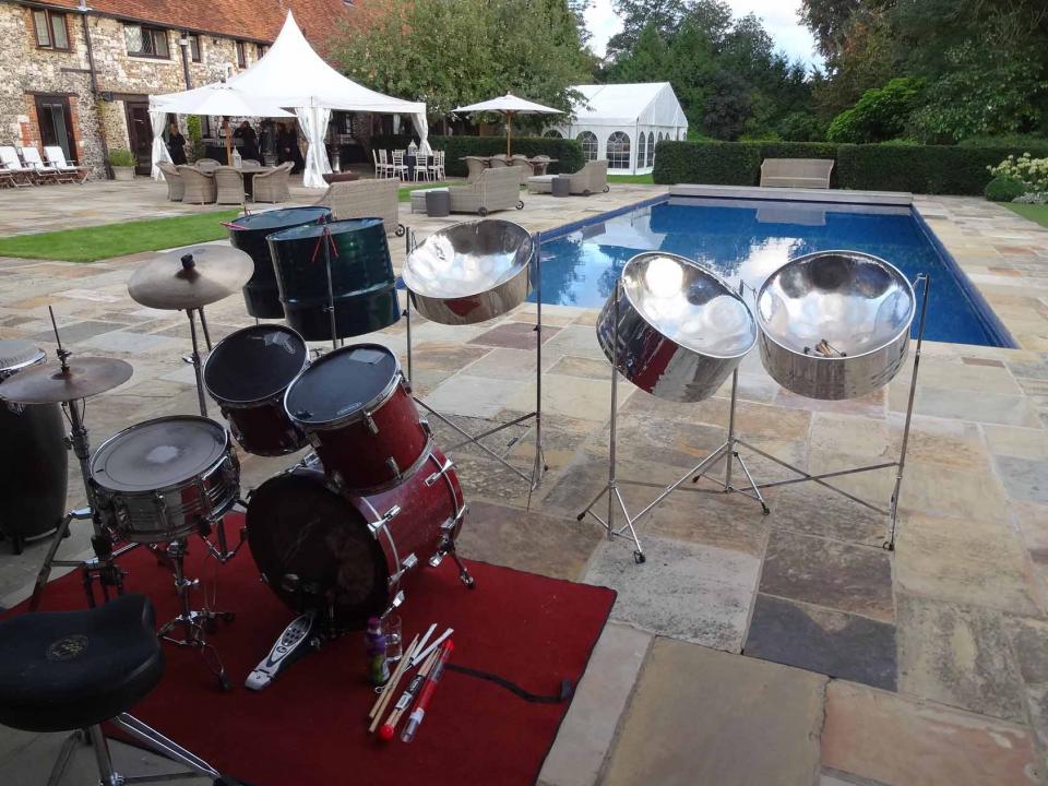 Caribbean steel drum band performing live at a luxurious private mansion in Marlow, with guests enjoying music by the poolside under sunny skies.